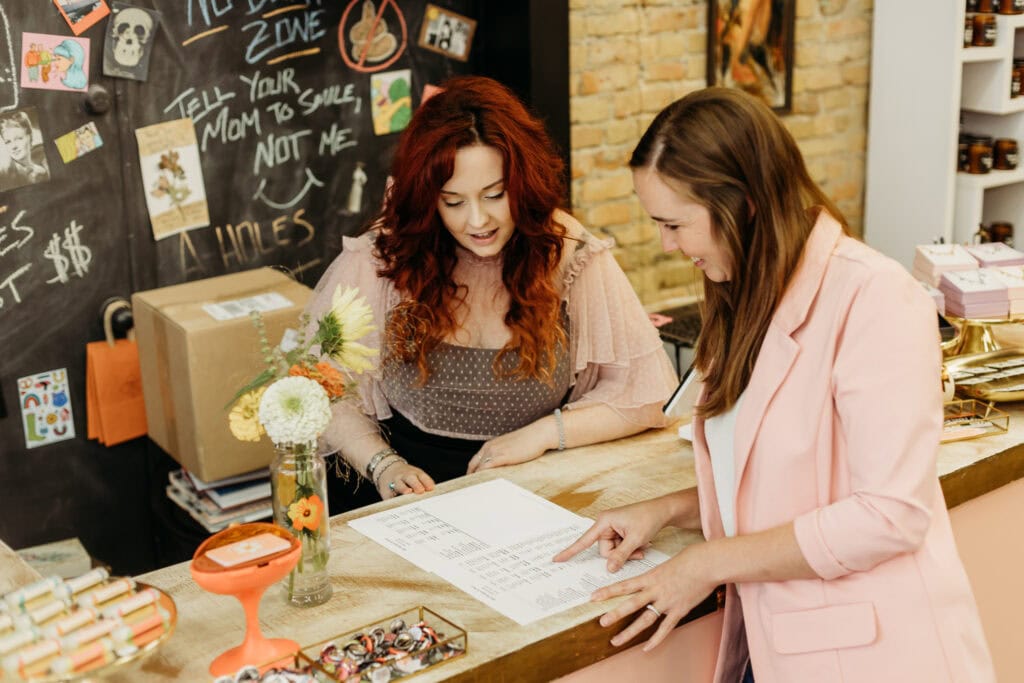 Two women discussing a document in a colorful retail shop with various items and decorations around them.